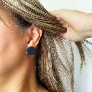 Model wearing a 20mm matte black round stud earring handmade from polymer clay by Vertseas.