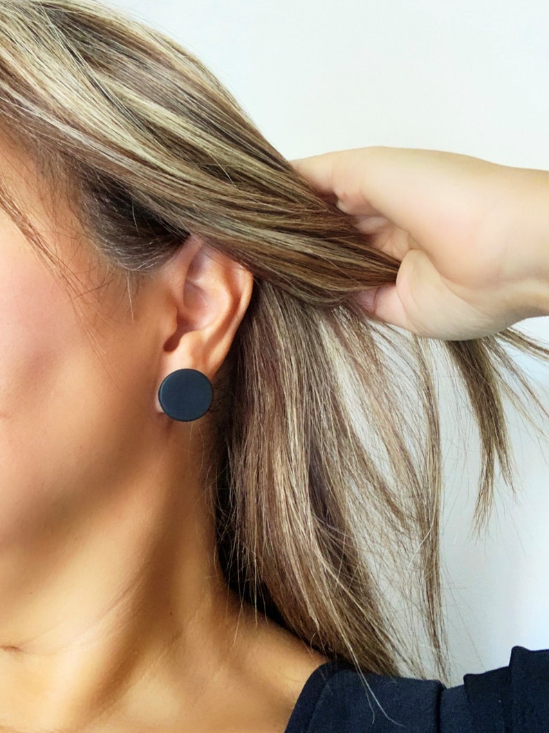 Model wearing a 20mm matte black round stud earring handmade from polymer clay by Vertseas.