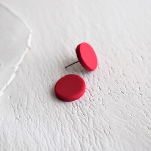 Könnte beinhalten: Ein Paar rote runde Ohrstecker. Die Ohrringe sind aus einem glatten, matten Material gefertigt.