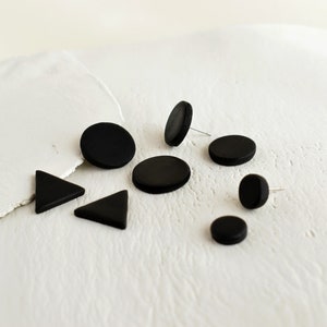 Display of matte black stud earrings handmade from polymer clay by Vertseas in different sizes and shapes.