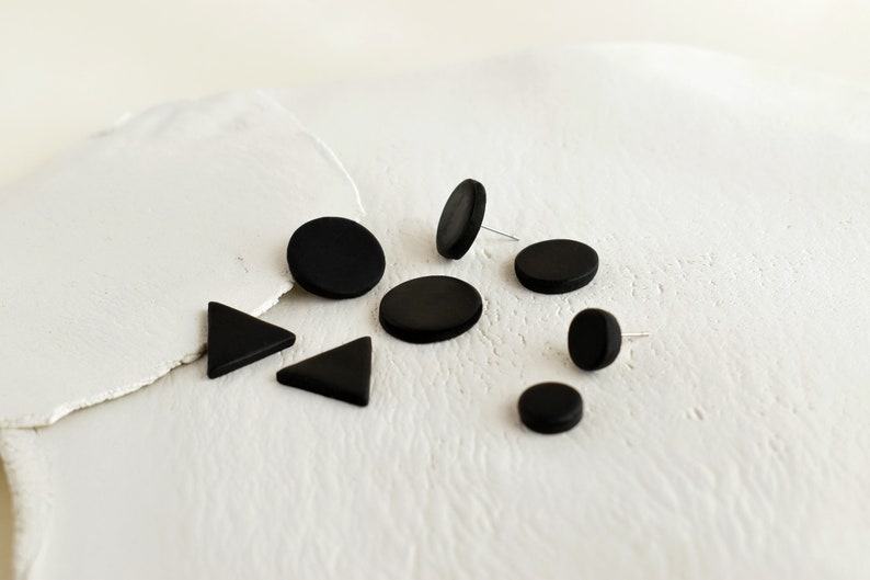 Display of matte black stud earrings handmade from polymer clay by Vertseas in different sizes and shapes.