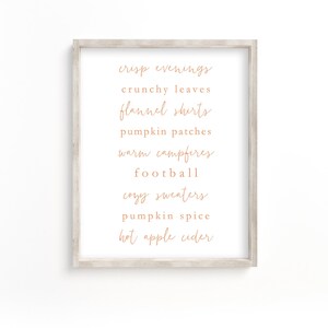 May include: A framed print with a list of fall-themed words in a handwritten font, including "crisp evenings", "crunchy leaves", "flannel shirts", "pumpkin patches", "warm campfires", "football", "cozy sweaters", "pumpkin spice", and "hot apple cider".