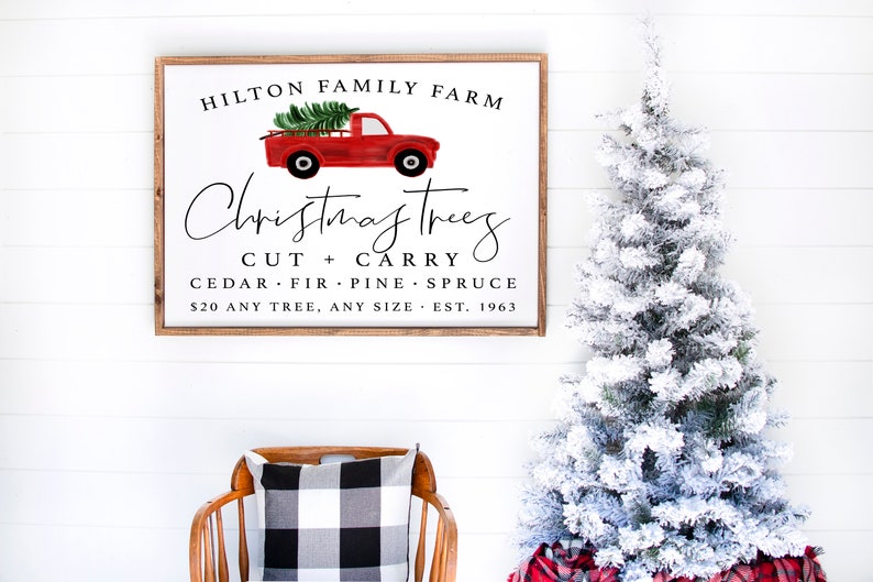 May include: A white sign with brown wood framing, advertising Christmas trees for sale at Hilton Family Farm. The sign features a red pickup truck with a Christmas tree in the bed. The text reads: "Hilton Family Farm, Christmas Trees, Cut + Carry, Cedar, Fir, Pine, Spruce, $20 Any Tree, Any Size, Est. 1963."