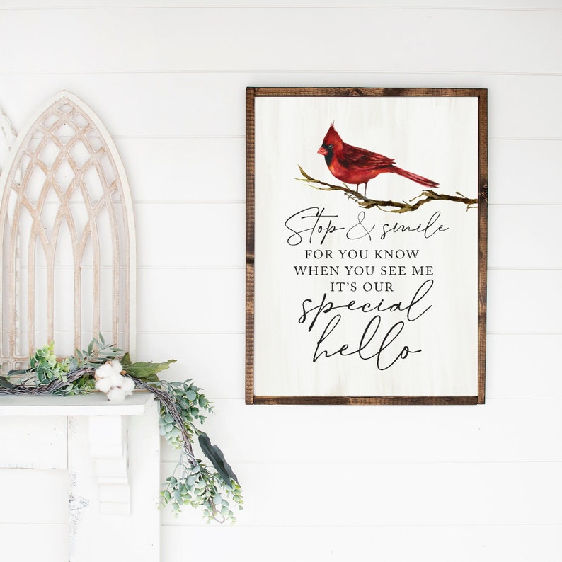 May include: A white wooden sign with a brown frame features a red cardinal perched on a branch. The sign reads "Stop & smile for you know when you see me it's our special hello".