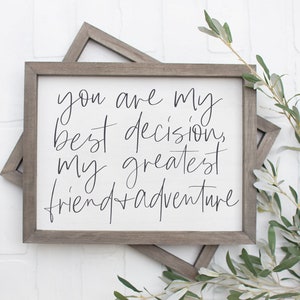 May include: A framed sign with the text "You are my best decision, my greatest friend + adventure" in black script font on a white background.