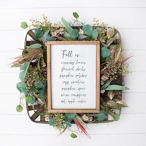 May include: A framed sign with the text "Fall is... crunchy leaves, flannel shirts, pumpkin patches, cozy sweaters, pumpkin spice, warm campfires, hot apple cider" surrounded by a wreath of green leaves.