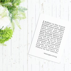 May include: A white card with black text on a white wooden background. The text reads: "A mother is the truest friend we have, when trials, heavy and sudden fall upon us; when adversity takes the place of prosperity; when friends desert us; when trouble thickens around us, still will she cling to us and endeavor by her kind precepts and counsels to dissipate the clouds of darkness, and cause peace to return to our hearts. -Washington Irving"