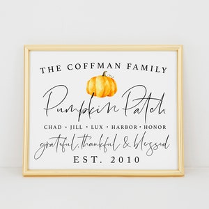 May include: A framed print with a white background and black text that reads "The Coffman Family Pumpkin Patch Chad Jill Lux Harbor Honor Grateful Thankful & Blessed Est. 2010". A watercolour painting of an orange pumpkin is above the text.