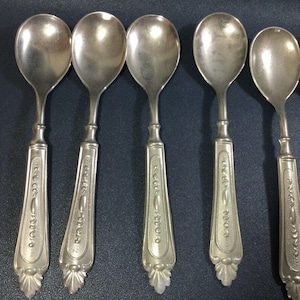 Puede incluir: Seis cucharas de plata con mangos ornamentados. Las cucharas tienen un cuenco redondeado y un diseño decorativo en el mango.