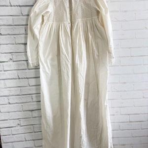 May include: A long-sleeved, floor-length off-white nightdress featuring a high collar and a front button closure. The upper bodice is detailed with intricate eyelet embroidery, while the cuffs are finished with delicate lace trim.