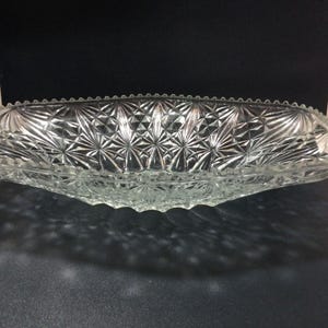 Puede incluir: Un bol de servir de vidrio transparente con un patrón de diamante. El bol tiene forma ovalada y tiene un borde festoneado.
