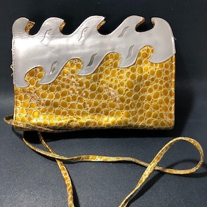 May include: A gold and silver clutch purse with a wave design. The purse has a long strap and a crocodile-embossed texture.