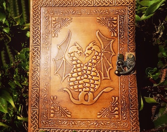 May include: A brown leather journal with a tooled design of two dragons intertwined. The journal has a metal clasp closure.