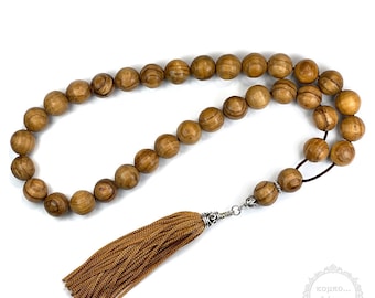 Puede incluir: Un collar de cuentas de oración de madera marrón con un borla marrón. Las cuentas son redondas y tienen un patrón de veta de madera natural. La borla está hecha de una tela suave y marrón.