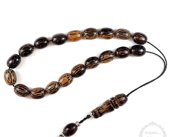 Puede incluir: Un collar de cuentas de oración de madera marrón con un borla negro. Las cuentas son de forma ovalada y tienen un patrón rayado. El collar tiene una cuenta de madera en el extremo con un acento plateado.