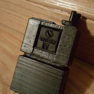 May include: A black plastic 3D printed object with a small, round, black button and the text "CRUISER" printed on it.