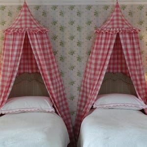 May include: Two twin beds with pink and white gingham canopy mosquito nets, white bedding, and matching headboards. Each bed has a bedside table with a lamp.