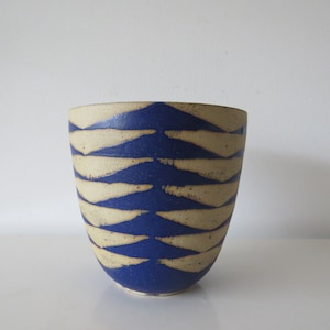Könnte beinhalten: Eine blaue Keramikvase mit einem weißen geometrischen Muster. Die Vase hat einen abgerundeten Boden und eine breite Öffnung.