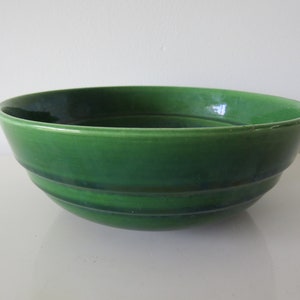 May include: A large, green ceramic bowl with a slightly rippled surface. The bowl is glazed and has a smooth, glossy finish.