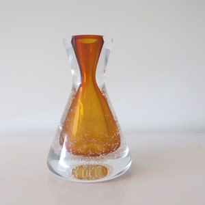 May include: A clear glass vase with a textured surface and an amber colored glass insert. The vase has a rounded base and a narrow neck.