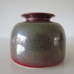 May include: A round ceramic vase with a green and red glaze. The vase has a wide mouth and a narrow neck.