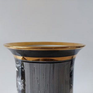 May include: Black and white ceramic vase with gold trim. The vase has a geometric pattern and a white design on the front.