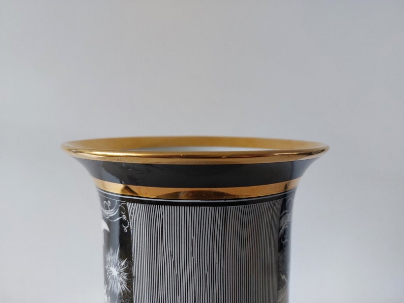 May include: Black and white ceramic vase with gold trim. The vase has a geometric pattern and a white design on the front.