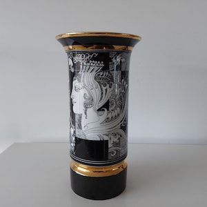 May include: Black and white ceramic vase with a gold rim and base. The vase features a detailed illustration of a woman's profile with intricate patterns and designs.