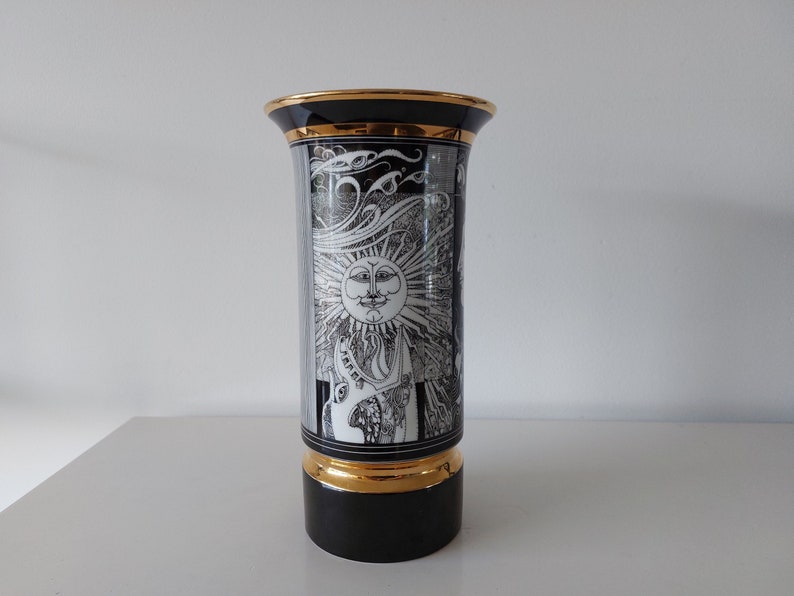 May include: Black and white ceramic vase with a gold rim and base. The vase features a stylized sun with a face and rays, and the word "Taurus" is visible on the side.