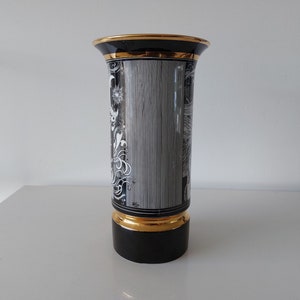 May include: Black and white ceramic vase with gold trim and a floral design. The vase has a cylindrical shape and a wide mouth.