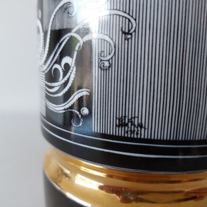 May include: Black and white ceramic vase with a gold trim. The vase has a geometric pattern with a stylized floral design. The vase is signed "W.H. 1972".