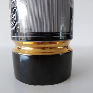 May include: Black and white ceramic vase with a gold trim. The vase has a geometric pattern and a black base.