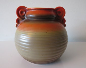 May include: A ceramic vase with a rounded body and two decorative handles. The vase is glazed in shades of brown, orange, and yellow.