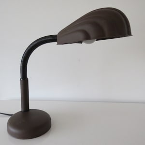 Peut inclure: Une lampe de bureau brune avec un bras flexible et un abat-jour incurvé. La lampe a un design simple et est en métal.