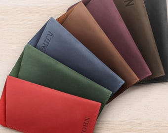 Peut inclure: Une collection d'étuis à lunettes personnalisés en cuir de différentes couleurs, dont le rouge, le vert, le bleu et le marron. Chaque étui est gravé d'un nom ou d'initiales, comme "JOHN" et "EMILY". Les étuis sont disposés en éventail sur une surface en bois clair.