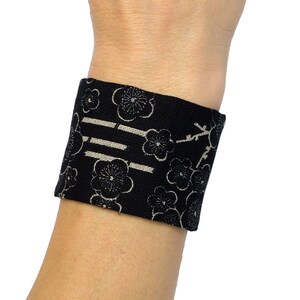 Peut inclure: Bracelet de poignet en tissu noir avec un motif floral blanc et un design rayé subtil.