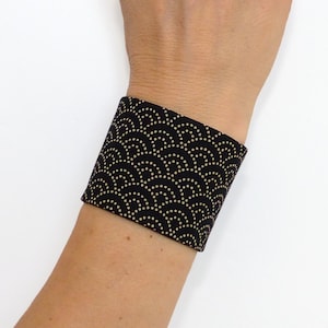 Op de afbeelding: Zwarte stoffen armband met een gouden patroon van overlappende cirkels en stippen.