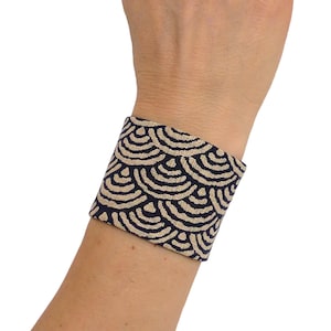 Peut inclure: Un bracelet de poignet en tissu noir et beige avec un motif géométrique. Le bracelet est fait d'un tissu doux et tissé et a un design simple et élégant.