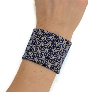 Può includere: Un braccialetto da polso in tessuto blu navy e beige con un motivo geometrico a stelle.
