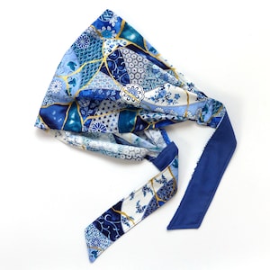 Puede incluir: Banda para la cabeza de tela azul y blanca con ribete azul. La tela presenta un diseño geométrico con detalles dorados.