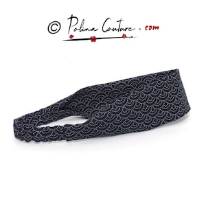 May include: A navy blue headband with a gold and white wave pattern. The headband is made of stretchy fabric and is designed to be worn around the head.