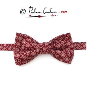 May include: A burgundy bow tie with a geometric pattern of white stars. The bow tie is made of fabric and has a classic shape.