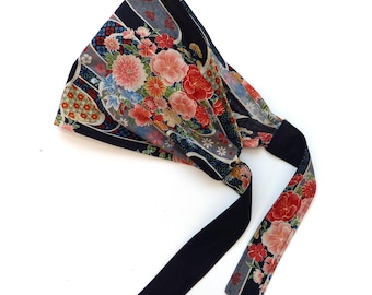 May include: A dark blue headband with a floral pattern in red, pink, and yellow. The headband has long, dark blue ties. The floral pattern includes various flowers and leaves.