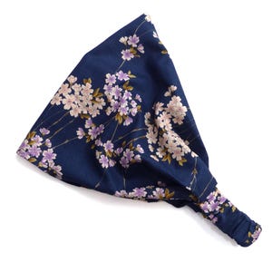 May include: A navy blue headband with an elastic back, adorned with a floral pattern of pink and purple blossoms and green leaves. The headband is made of soft fabric and is designed for comfort and style.