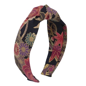 May include: A black headband with a knotted design. The headband is covered in a floral print with red, pink, gold, and purple flowers on a black background.