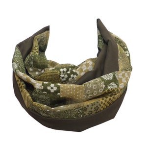 Könnte beinhalten: Ein dunkelolivgrüner und gemusterter Stoff-Cowl-Schal. Der Schal hat ein Patchwork-Design mit verschiedenen Grüntönen, Weiß und Beige mit floralen und geometrischen Mustern. Die Kanten sind einfarbig dunkelolivgrün.