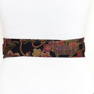 May include: A black fabric belt with a gold and burgundy floral pattern. The belt is tied around a white mannequin.