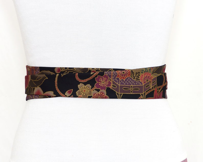 May include: A black fabric belt with a gold and burgundy floral pattern. The belt is tied around a white mannequin.