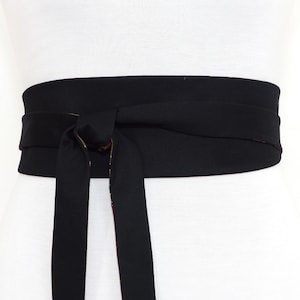 May include: A black fabric belt with a wide, flat design. The belt is tied in a bow at the front.
