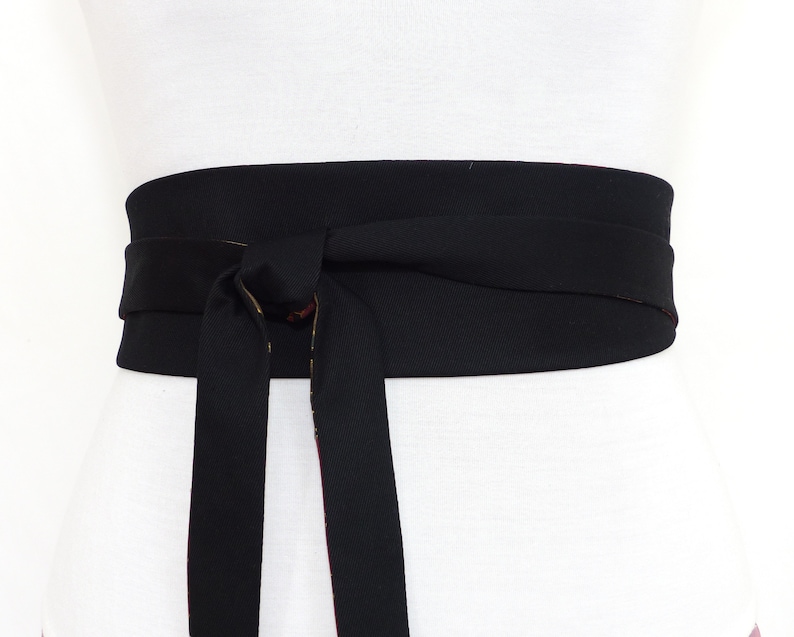 May include: A black fabric belt with a wide, flat design. The belt is tied in a bow at the front.